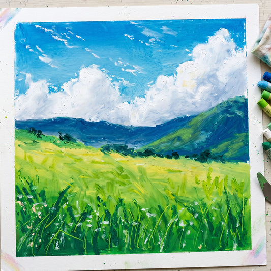 Handcrafted square oil pastel painting of a summer meadow with vibrant green grass, mountains, and fluffy white clouds.